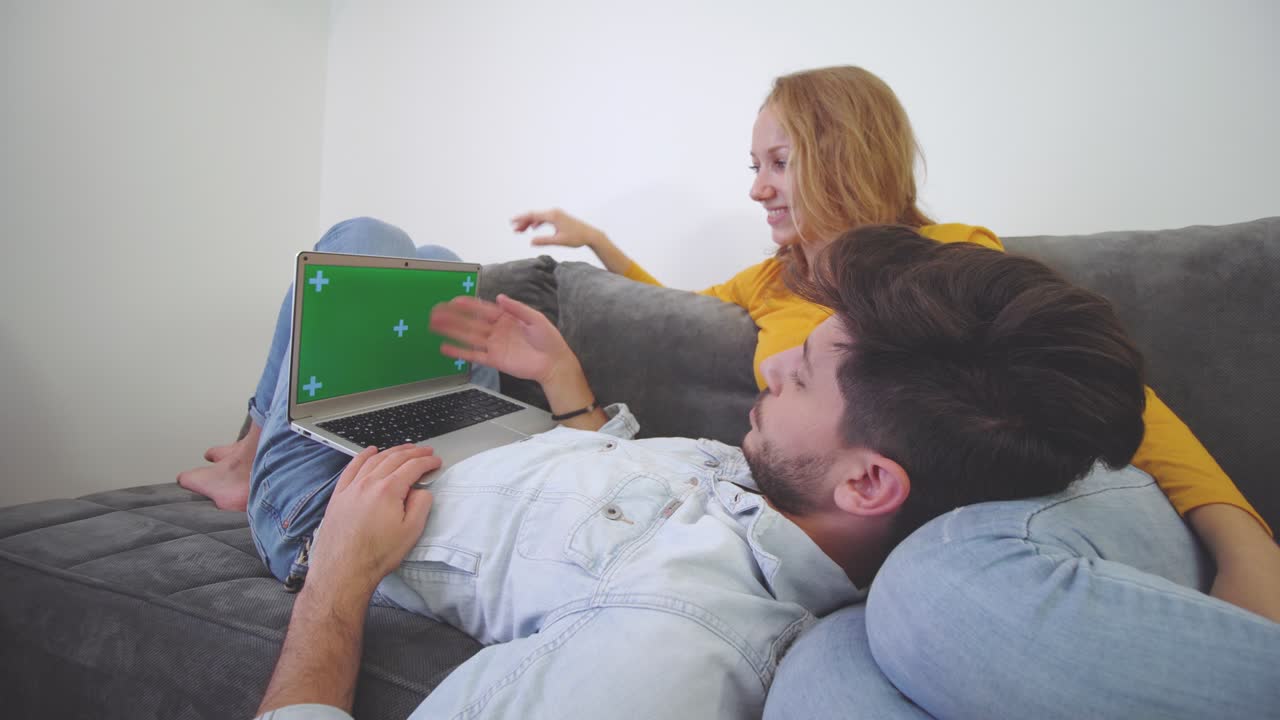 влюбленная пара на диване смотрит на ноутбук. мальчик лежит на коленях девушки. зеленый экран.