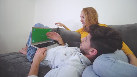 una pareja enamorada en un sofá mirando una computadora portátil. un niño tendido en el regazo de una niña. pantalla verde.