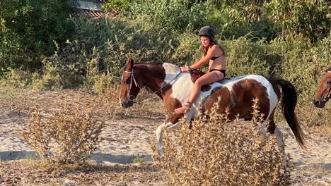 Young-girl-in-bikini-enjoys-bareback-riding-on-sandy-beach-without-saddle-on-hot-summer-day