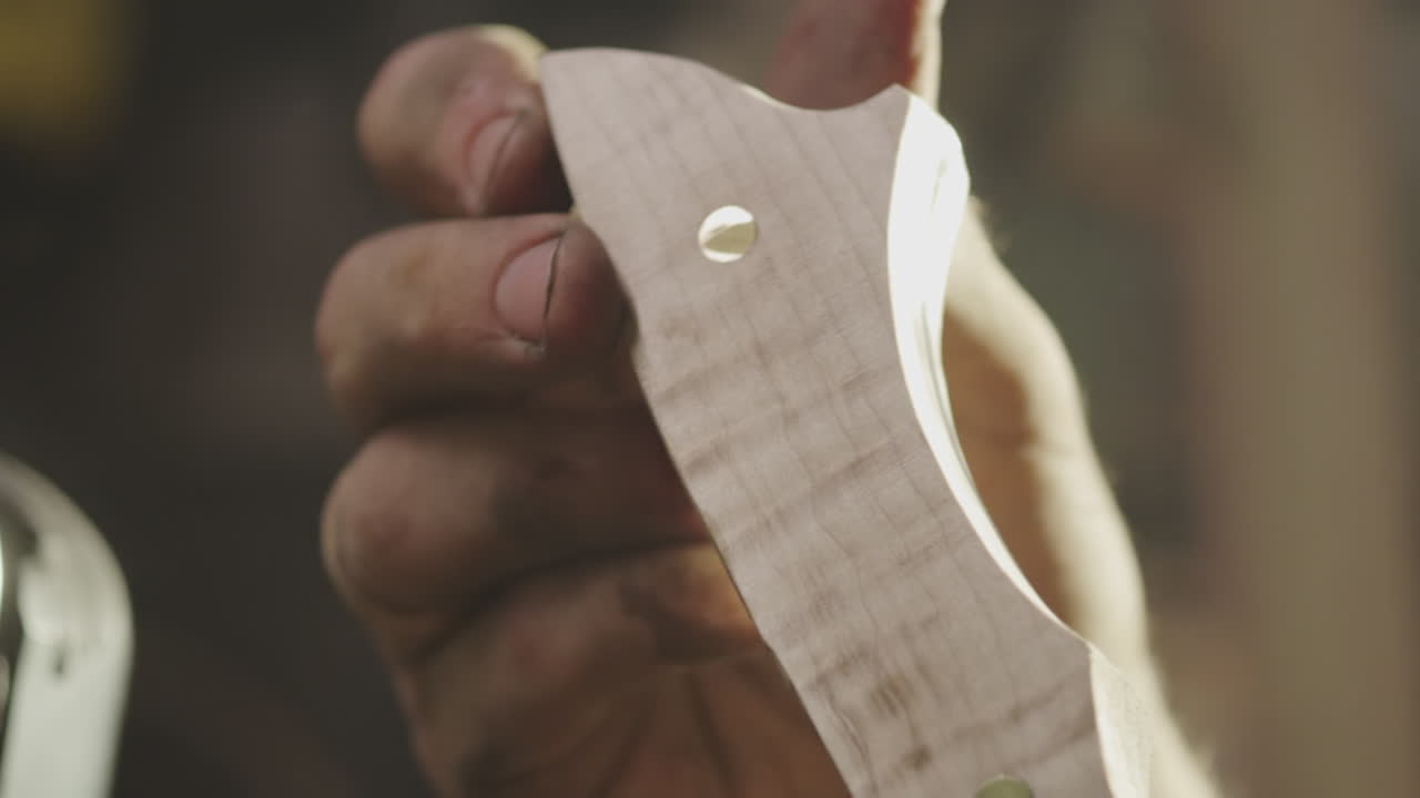 A man sands and smooths the wooden handle of a knife he made