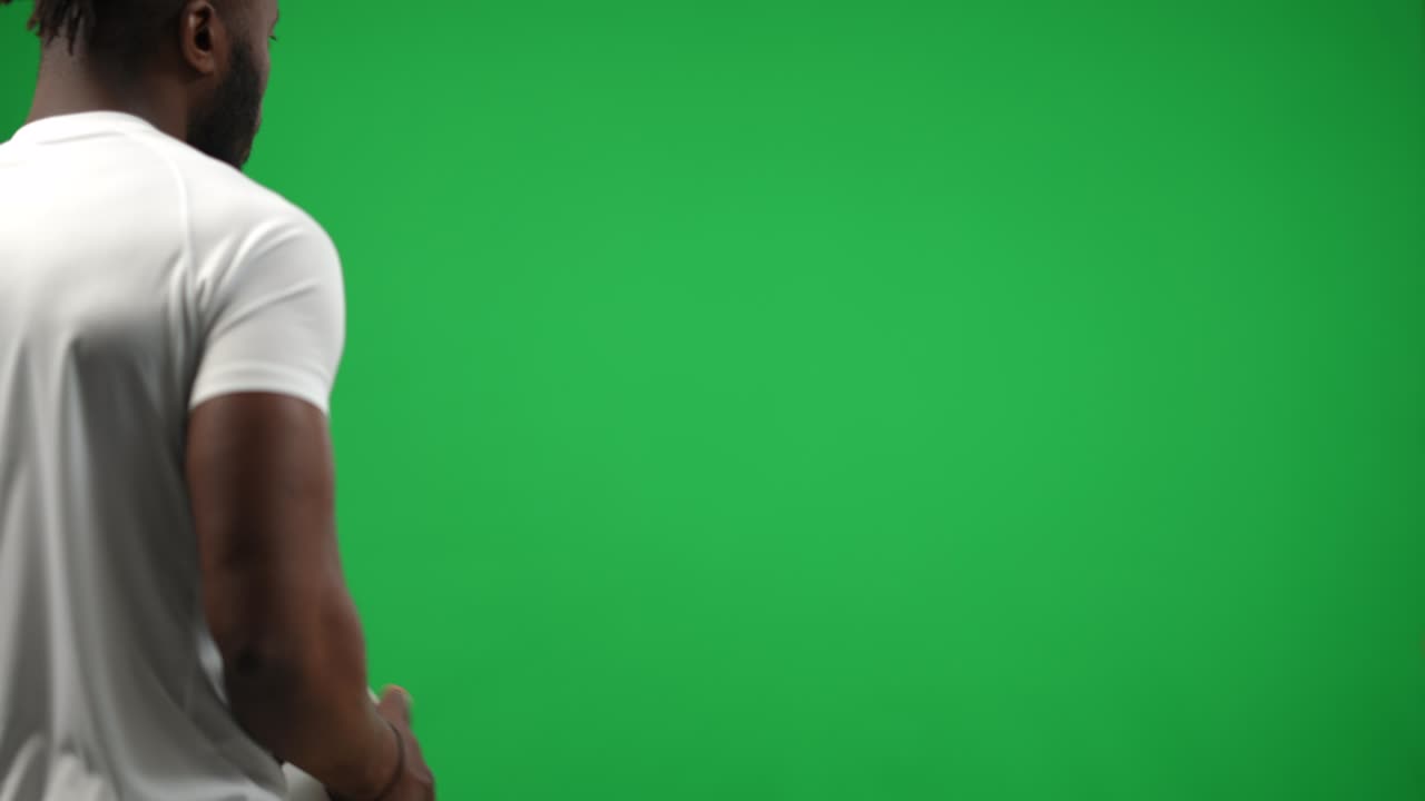 Jovem jogador de futebol afro-americano visto por trás caminhando na tela verde vindo da esquerda, passando a bola com as mãos. Atleta confiante jogando em fundo de chroma key. Conceito de campeonato de futebol.