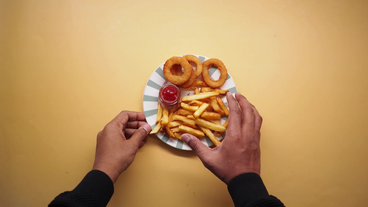 Mani che afferrano patatine fritte e anelli di cipolla da un piatto