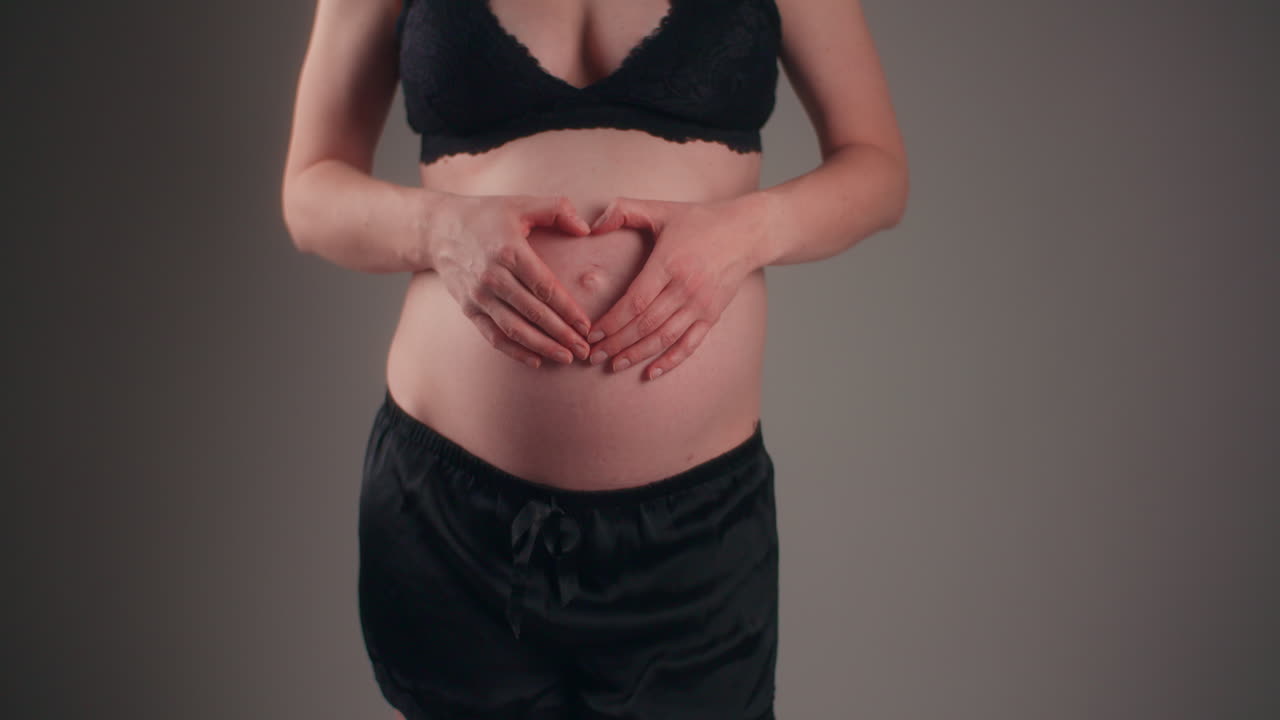 Mulher mostra símbolo de coração na barriga durante a gravidez
