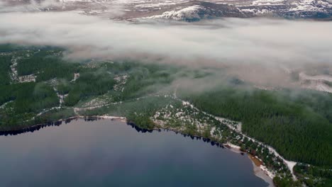 above verdant forest around lake shrouded in cloud surrounded by snowy mountains