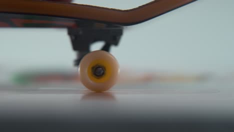 a hyper macro detailed shot of a mini skateboard, close-up on the tiny white wheels, riding fingerboard from right to left, finger slide, professional lighting, static cinematic 4k video