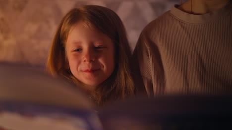 happy girl sits with mother listening to interesting book