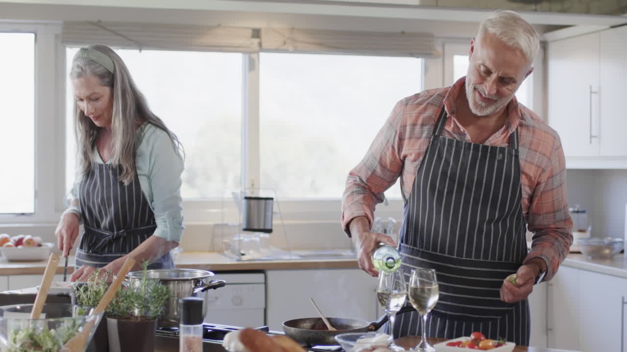 pareja caucásica de mediana edad vertiendo vino, preparando comida, cocinando en la cocina en casa, cámara lenta