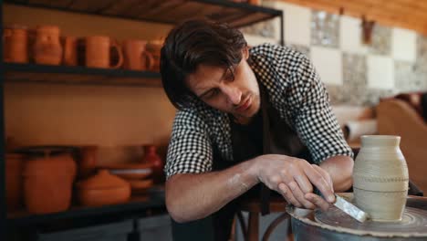 ceramist uses special tool on potter's wheel and creates a handmade clay product