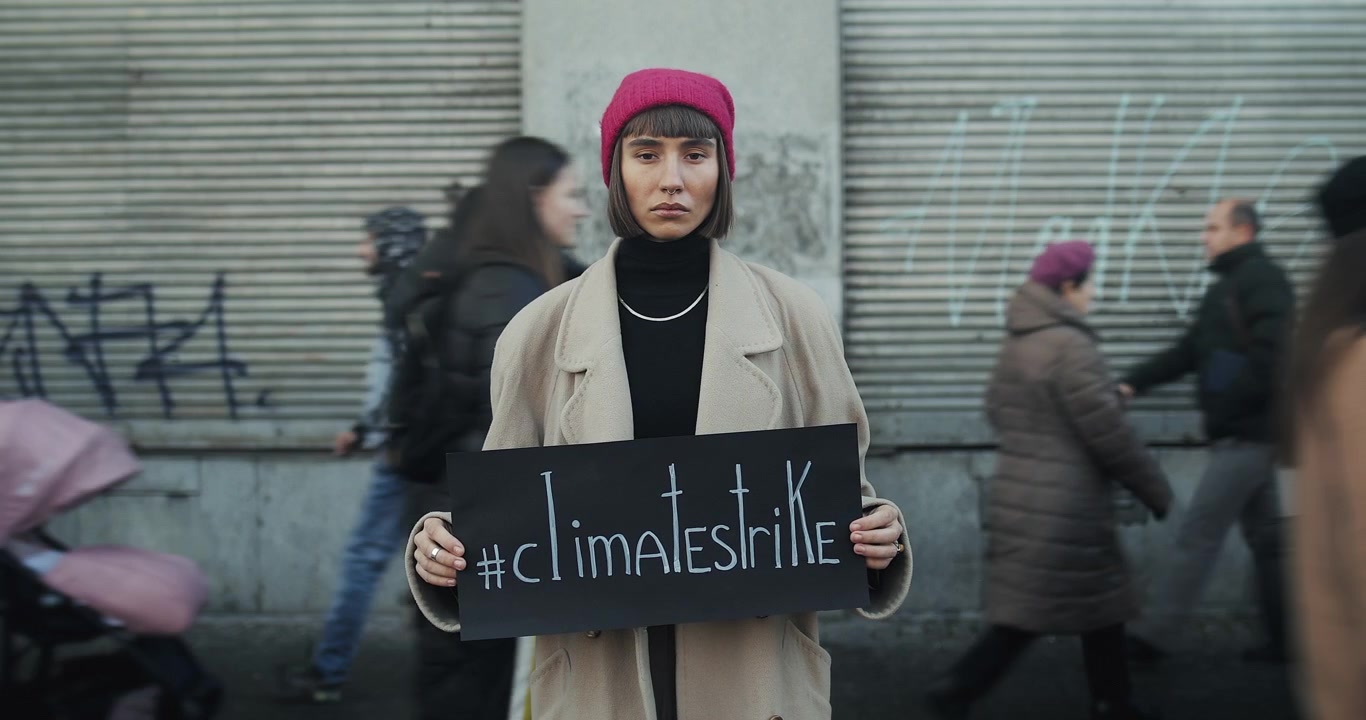 Mladá žena držící ceduli klimatické stávky na rušné městské ulici