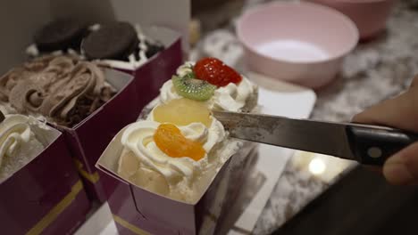 Close-Up-View-Of-Knife-Slicing-Fresh-Cake-Slices-Topped-With-Fresh-Fruit-In-Half