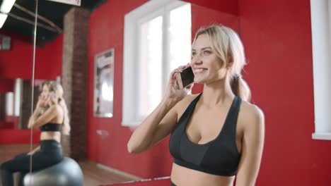 Fitness-woman-calling-mobile-phone-in-gym-club.-Young-woman-sitting-on-gym-ball