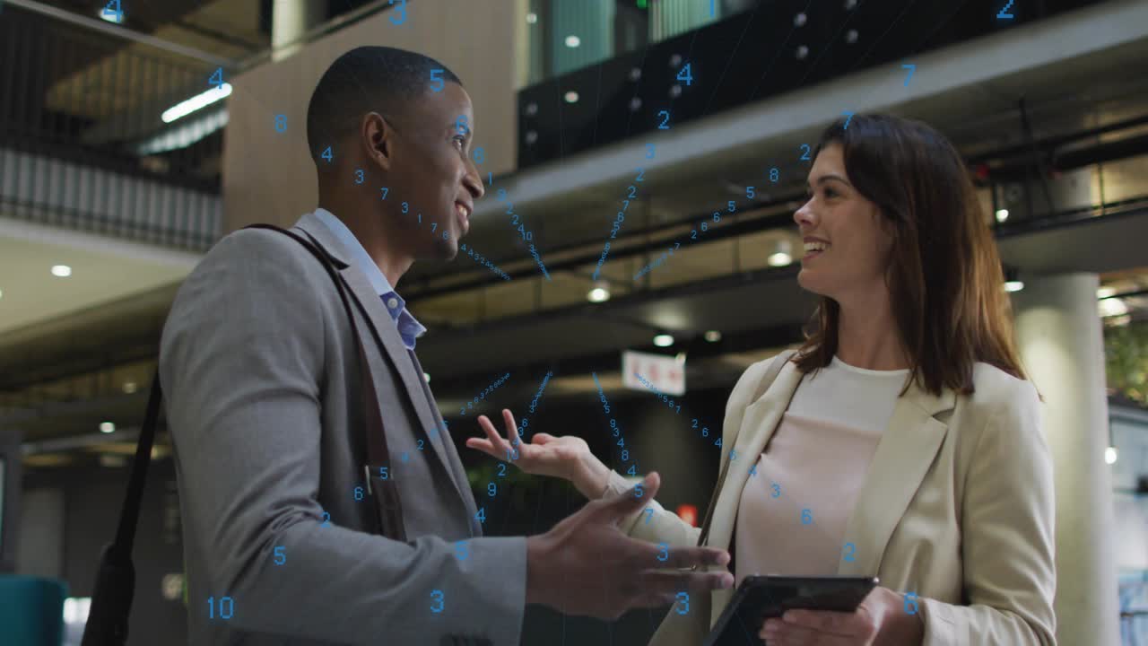 Two colleagues reviewing data in corporate atrium, woman tapping tablet and activating blue overlay
