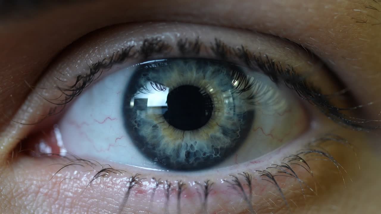 Filming tight eye closeup in room as light turns on, pupil constricting, showing iris and window