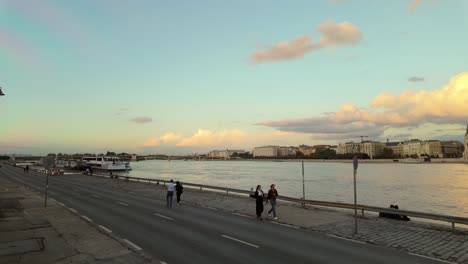 people walk on the lower quay closed from traffic due to flooding in budapest with the margaret bridge in the background after sunset in hungary.