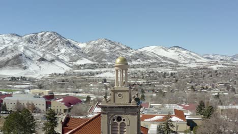 An-aerial-drone-shot-orbiting-a-small-tower-in-the-middle-of-a-small-town-while-slowly-zooming-out-overlooking-snowy-mountains-in-the-winter