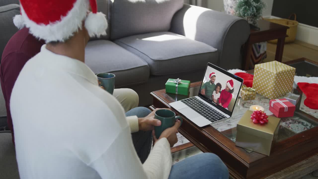 padre y hijo biraciales usando computadora portátil para una videollamada de navidad con familia feliz en la pantalla