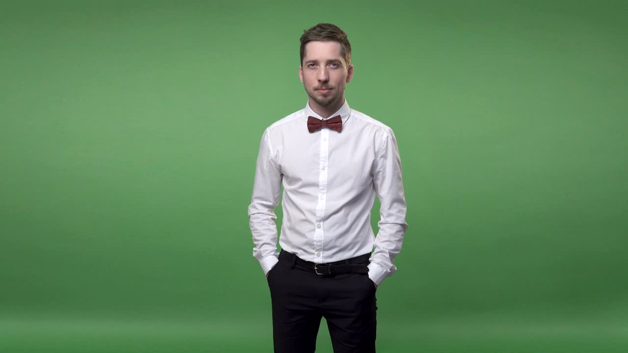 셔츠를 입은 잘생긴 젊은 남자가 주머니에 손을 넣고 서 있습니다. 크로마 키 녹색 화면 배경