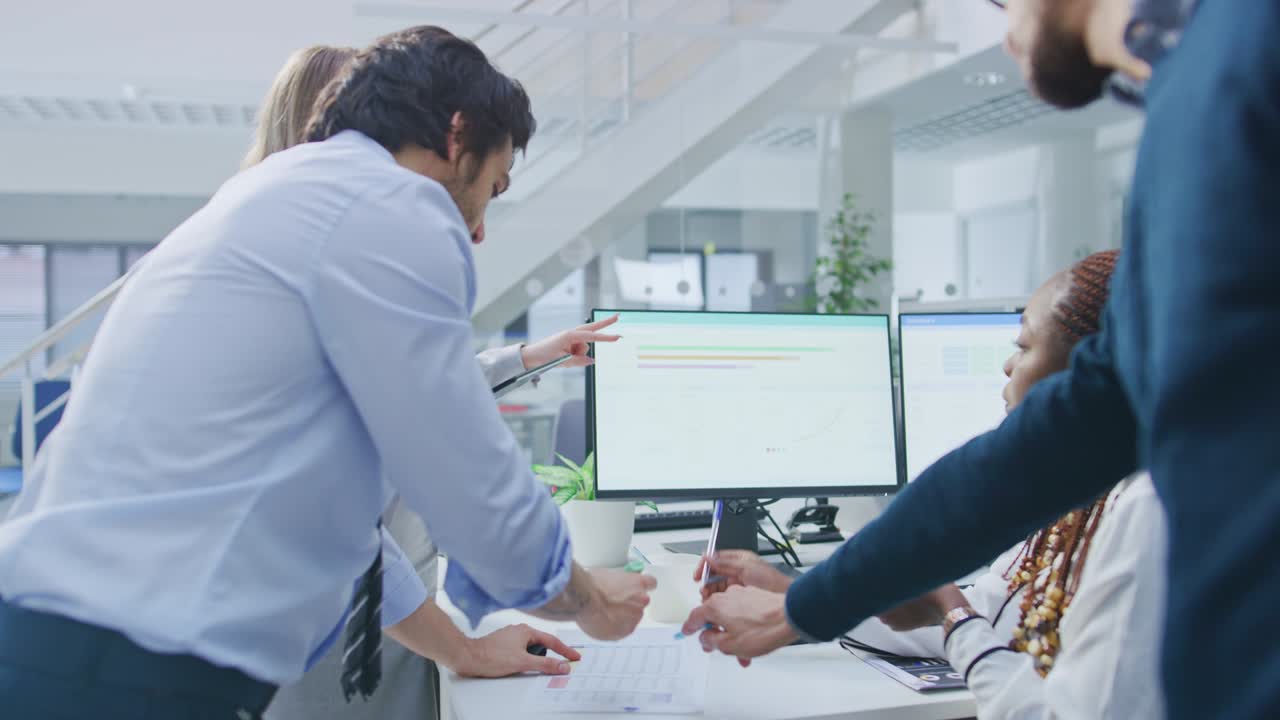 In the Bright Busy Office Group of Young Professionals have Team Building Meeting. Standing at the Desk, Discuss Problem Solutions, Planning and Strategizing, Use Digital Tablets and Desktop Computers