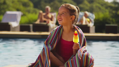 Familia-En-Vacaciones-De-Verano-Con-Una-Chica-Comiendo-Polo-De-Hielo-Al-Borde-De-La-Piscina