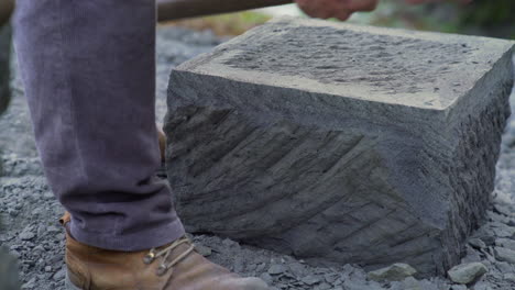 Tiro-De-Carro-De-Mano-De-Un-Artesano-De-Piedra-Usando-Un-Pico-Para-Bordear-Un-Gran-Ladrillo-De-Piedra,-En-La-Ciudad-De-Ancud,-En-La-Isla-De-Chiloé