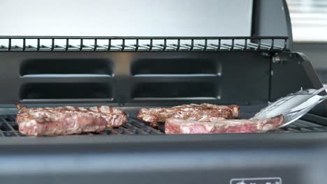 chef hand with metal pliers flipping pork ribs cooking on hot grill