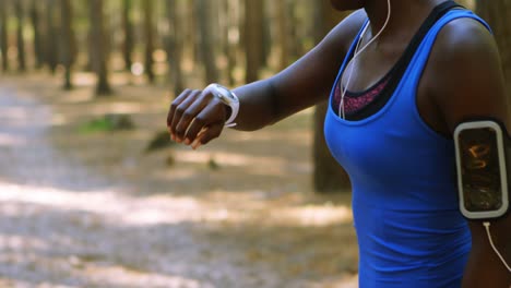 Female-jogger-checking-time-on-smartwatch-in-the-forest-4k