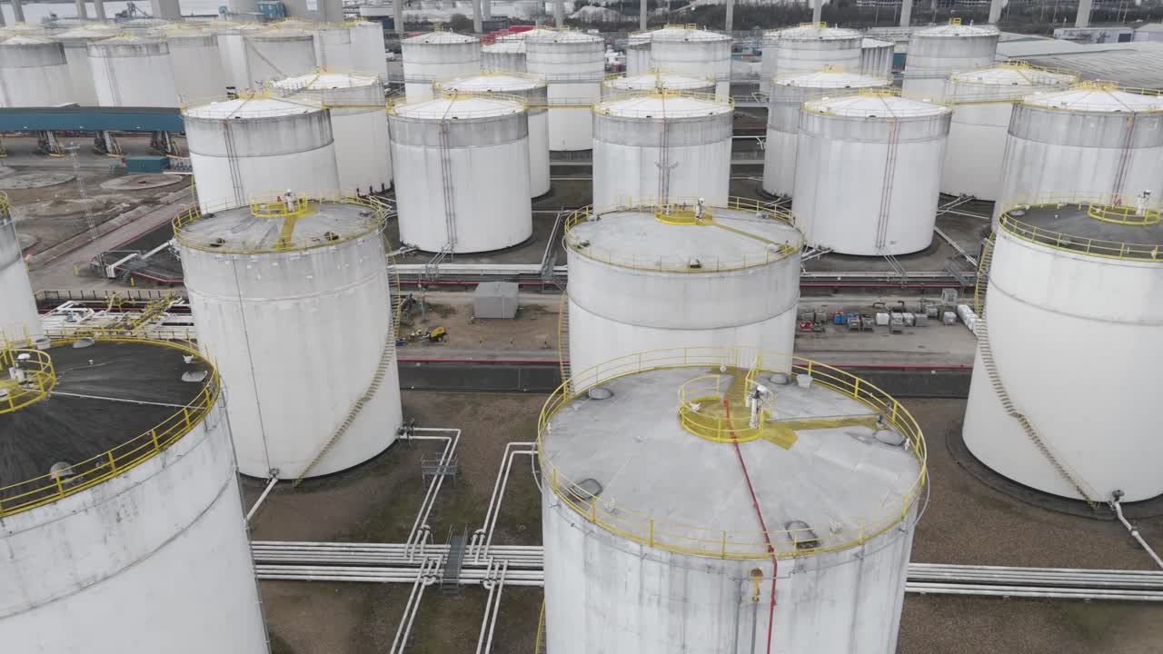 Top-down aerial of tightly packed white cylindrical fuel silos with safety railings, pipes and service catwalks lining Thames riverfront depot, conveying large-scale energy storage and petro-logistics