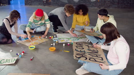 young environmental activists painting placards sitting on the floor