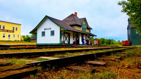 pioneer museum town with costumed people waiting at train station by hotel grain processing plant in north american vintage buildings signs railway seed car circa 1838-1938