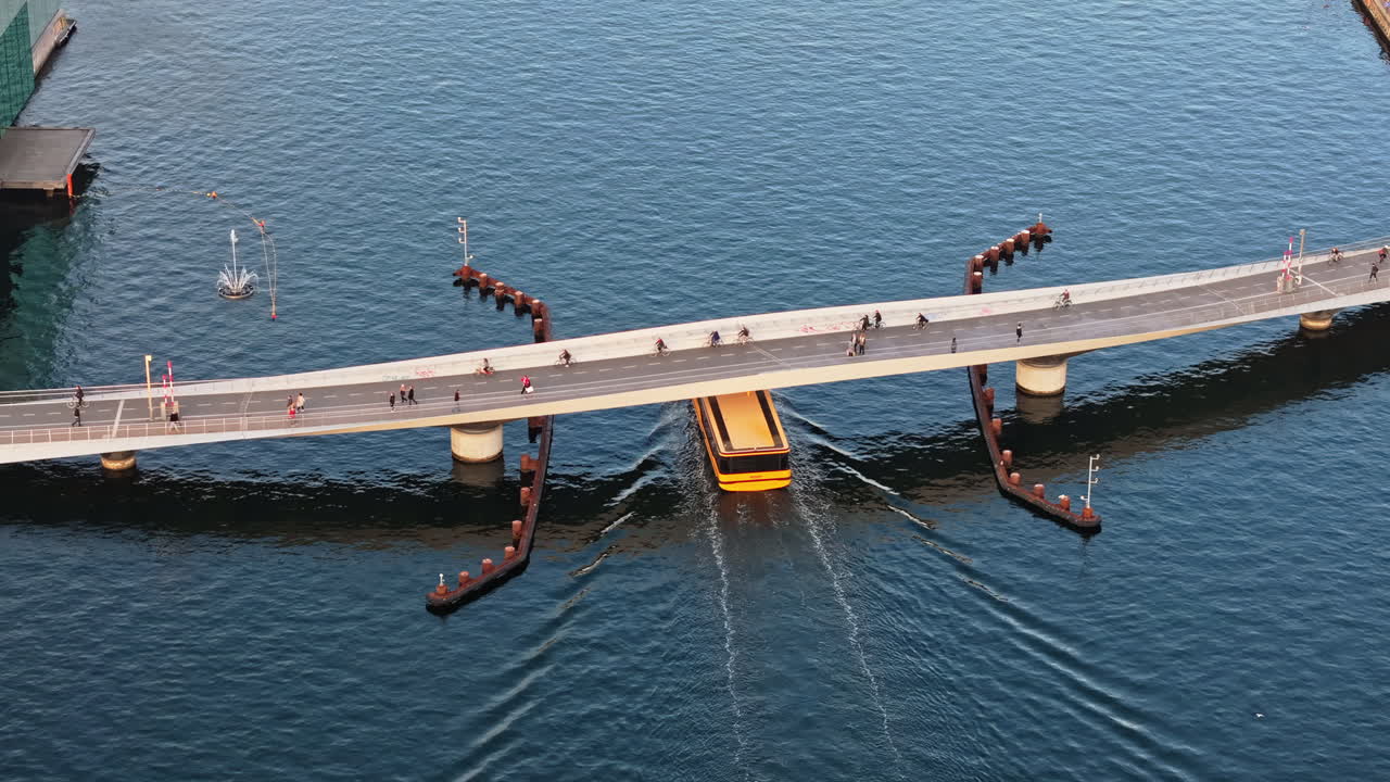 Aerial drone view of a yellow boat moving on the water under the Quay Bridge across the port of Copenhagen, Denmark in the evening