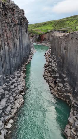 towering basalt columns and serene river in studlagil canyon, iceland, vertical shot