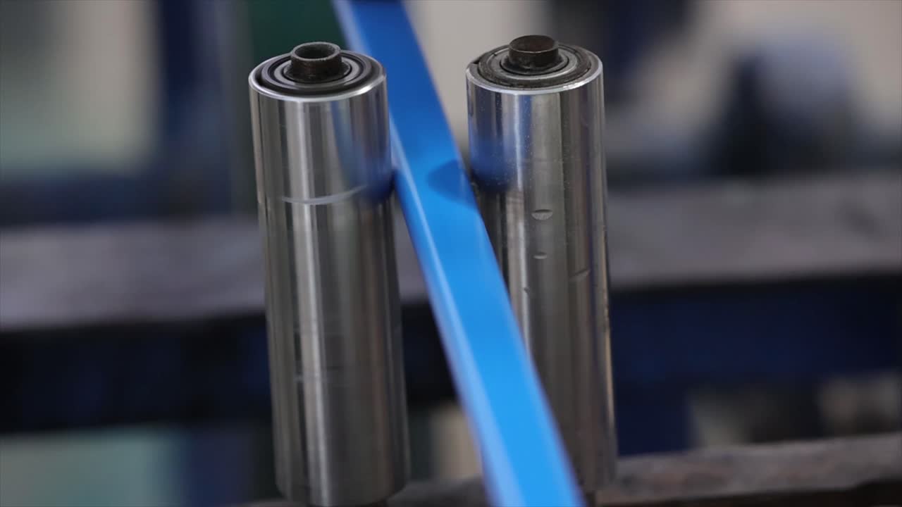 Automated industrial machinery guiding a vibrant synthetic material through a set of metal rollers