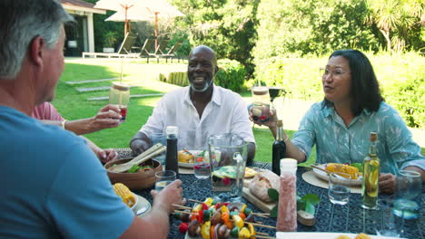 enjoying in garden lunch, diverse senior friends laughing and sharing drinks in garden
