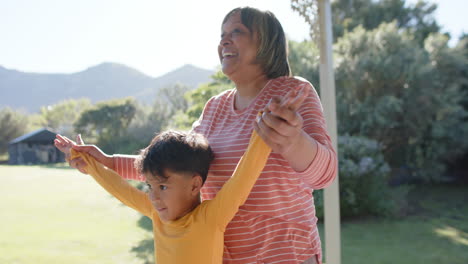 happy senior biracial grandmother and grandson doing yoga, meditating on terrace, slow motion
