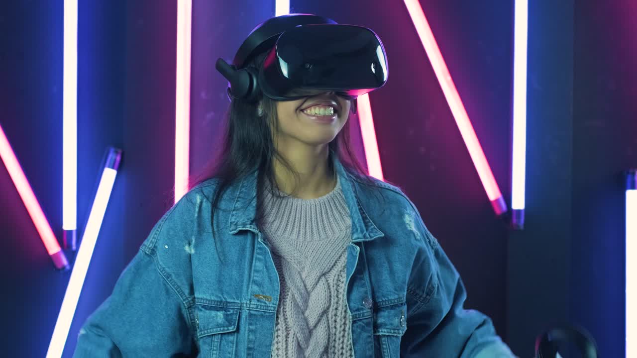 giovane donna che gioca e sorride nell'auricolare vr. casco di realtà virtuale sullo sfondo di illuminazione a colori