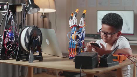 Asian Cute Boy Using Smartphone While Working About A Cyborg Hand On A Laptop At Home