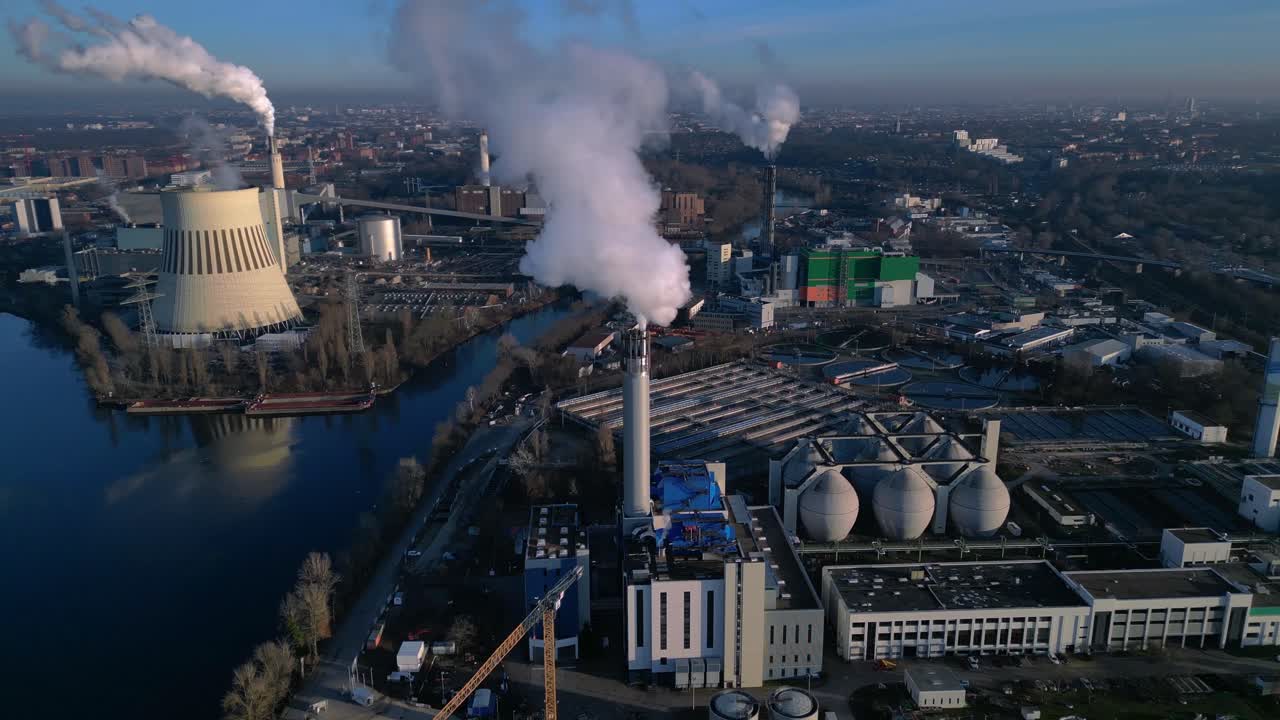 industrial heating plant with chimney releasing smoke into blue sky, impacting environment by a canal. Marvelous aerial view rotation pan to left drone