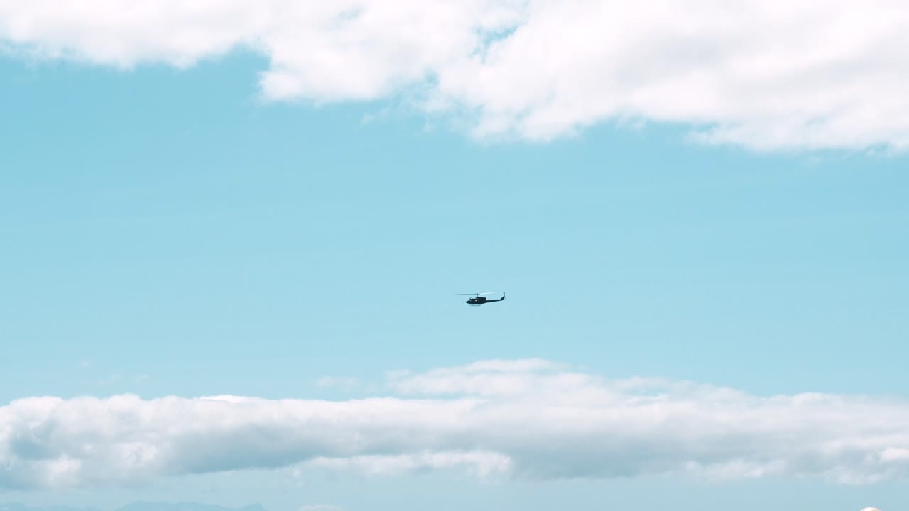 一架直升機在平靜的藍色海面上空巡邏海岸線的廣角鏡頭。