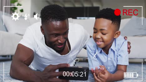 animation of lights over happy african american father and son recording video on smartphone