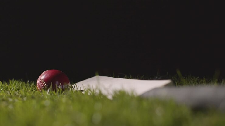 Natura morta di cricket in studio con primo piano di una palla che rotola su una mazza adagiata sull'erba