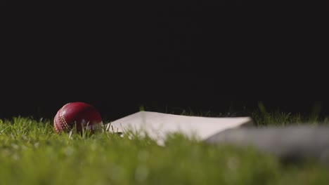 studio cricket still life with close up of ball rolling onto bat lying in grass