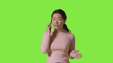 studio shot of frustrated woman talking on mobile phone against green screen