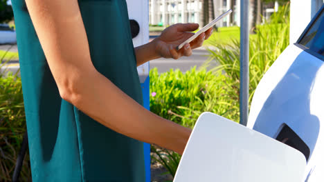 Woman-using-mobile-phone-while-charging-electric-car-4k