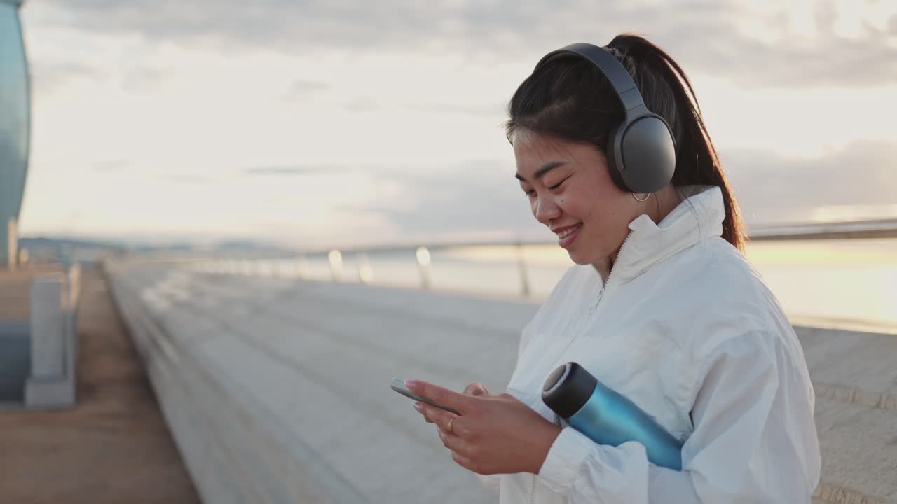 Donna sorridente con le cuffie che controlla il telefono su una passeggiata urbana