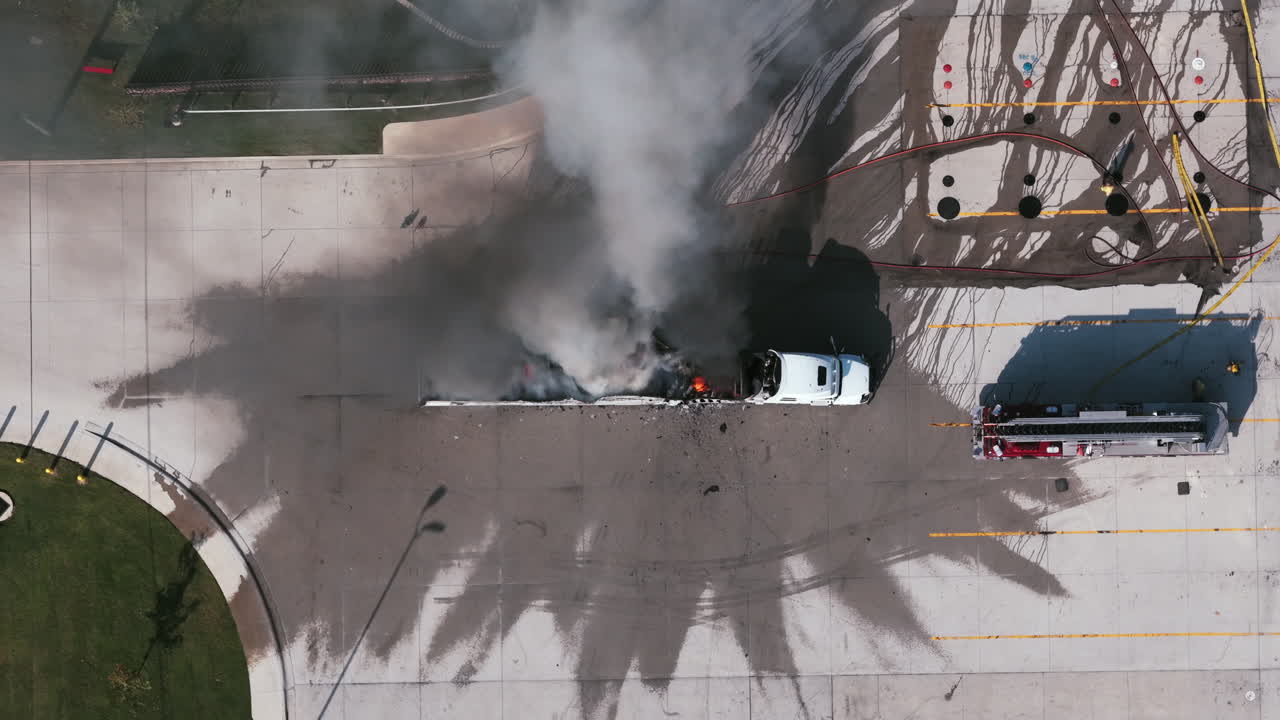 Image 3: Close-up aerial shot of a burning semi-truck in a parking lot with heavy smoke and flames as firefighters work to control the blaze
