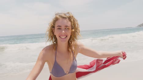 Front-view-of-Caucasian-woman-with-waving-American-flag-dancing-on-the-beach-4k