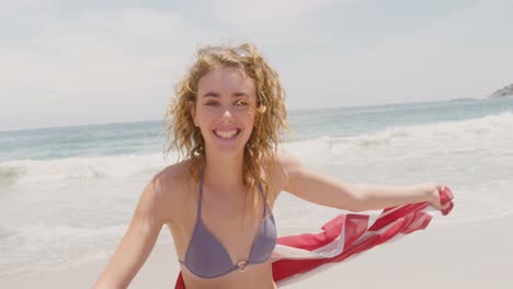 front view of caucasian woman with waving american flag dancing on the beach 4k