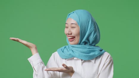 녹색 스크린 배경 스튜디오에 서서 웃고 을 가리키는 아시아 무슬림 여성의 클로즈업