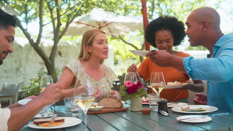 group of friends enjoying outdoor meal and wine on visit to vineyard restaurant