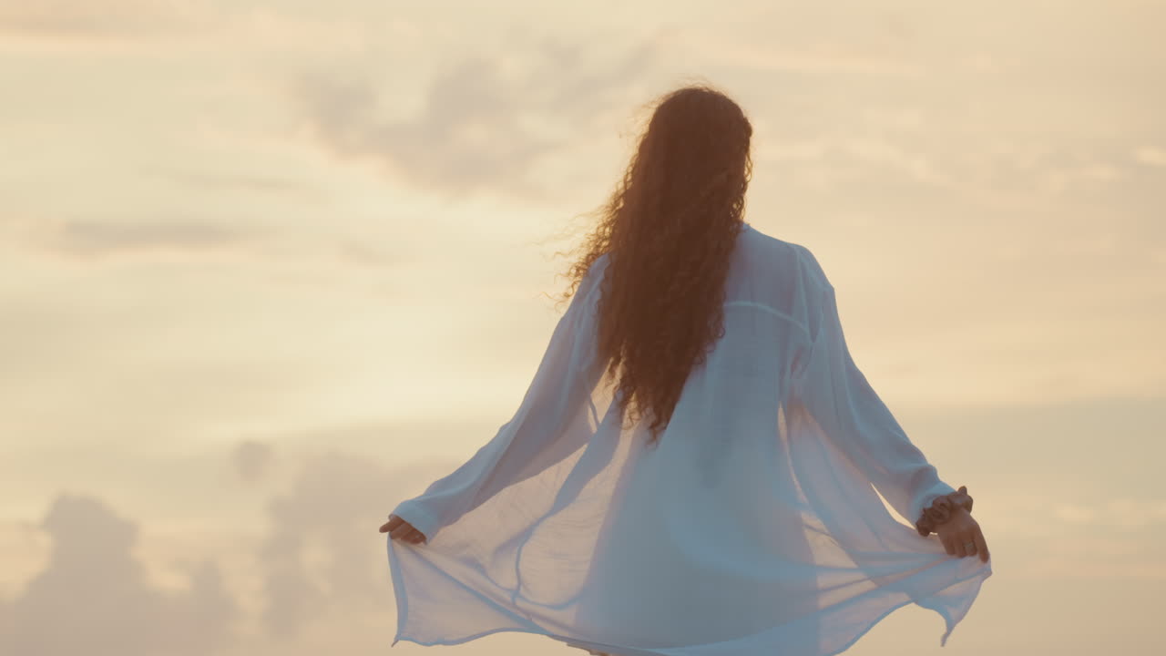 Senhora graciosa gira à beira-mar ao entardecer. Noite costeira serena com a senhora dançando livre e elegantemente. Mulher elegante executando giros ao longo da costa durante o brilho do crepúsculo com uma brisa suave do oceano.